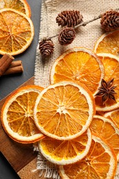 Photo of Many dry orange slices and spices on black textured table, flat lay