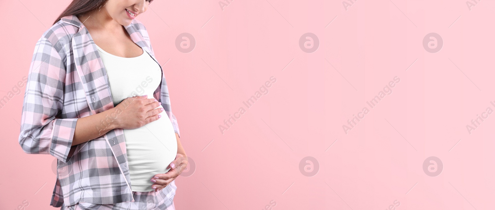 Image of Young pregnant woman holding hands on belly against color background, closeup view with space for text. Banner design