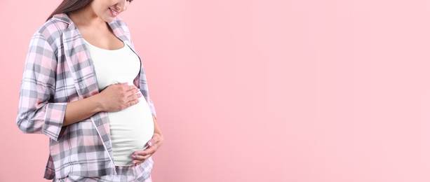 Young pregnant woman holding hands on belly against color background, closeup view with space for text. Banner design
