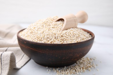 Dry barley groats and scoop in bowl on white table, closeup