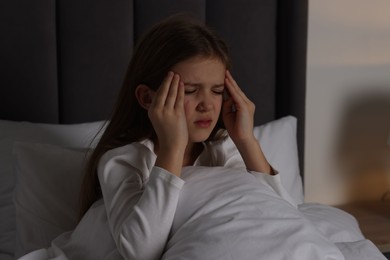Little girl suffering from headache in bed at night