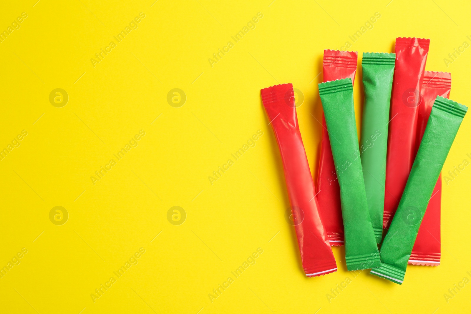 Photo of Different sticks of sugar on yellow background, flat lay. Space for text