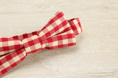 Stylish red and white gingham bow tie on wooden background, closeup