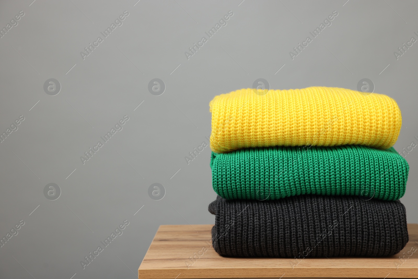 Photo of Stack of knitted sweaters on wooden table against grey background. Space for text