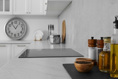 Photo of Different ingredients on white marble countertop near cooktop in kitchen. Interior design