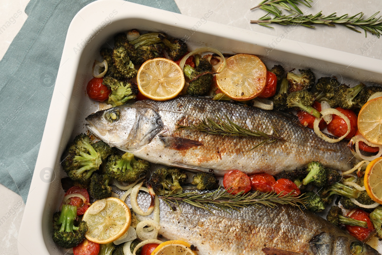 Photo of Delicious fish with vegetables and lemon in baking dish on light marble table, top view