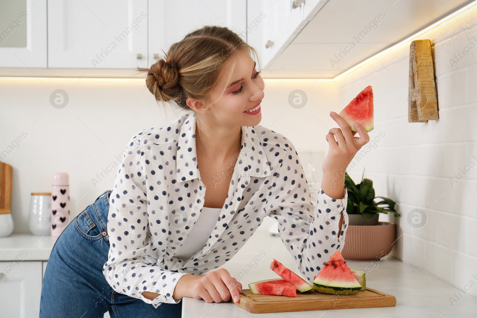 Photo of Beautiful teenage girl with slice of watermelon near countertop in kitchen