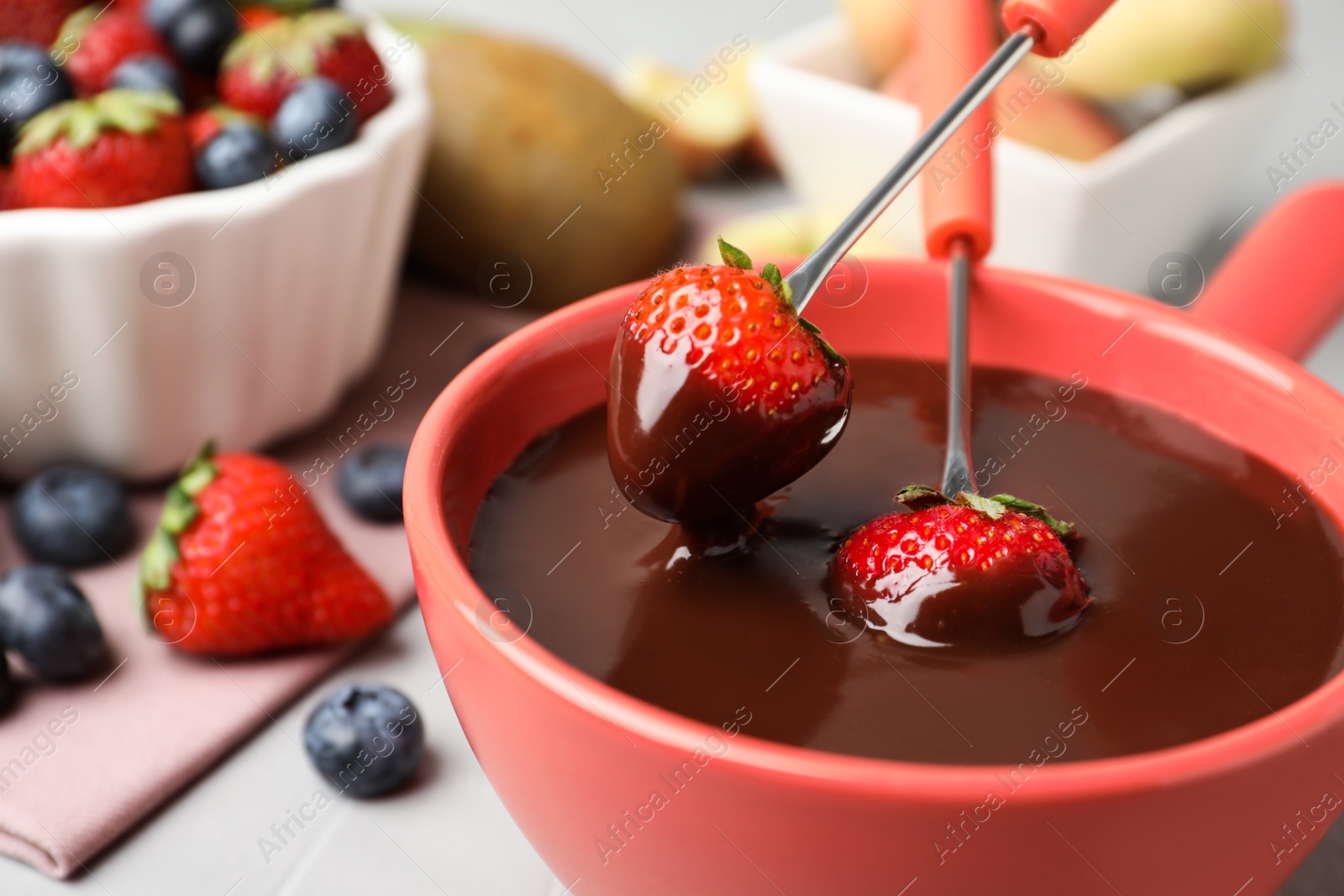 Photo of Dipping strawberries into fondue pot with chocolate on table, closeup