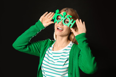 Young woman with party glasses on black background. St. Patrick's Day celebration