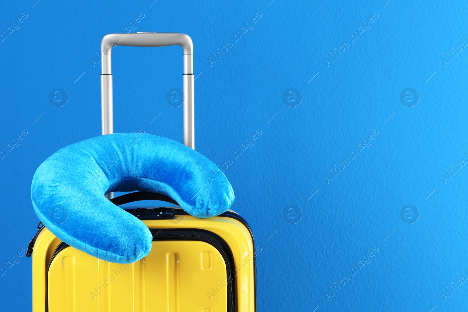 Photo of Yellow suitcase and travel pillow on blue background, space for text