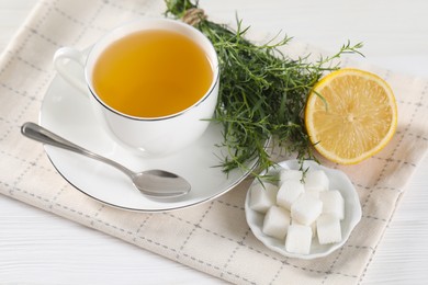 Aromatic herbal tea, fresh tarragon sprigs, sugar cubes and lemon on white wooden table