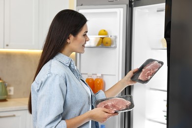 Photo of Young woman taking packs of meat out of refrigerator in kitchen