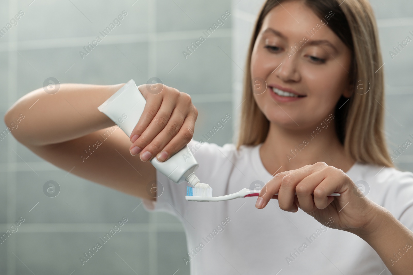 Photo of Young woman applying toothpaste onto brush in bathroom, focus on hands