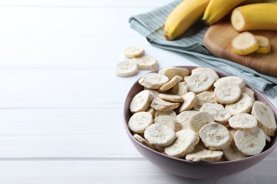 Photo of Freeze dried and fresh bananas on white wooden table. Space for text