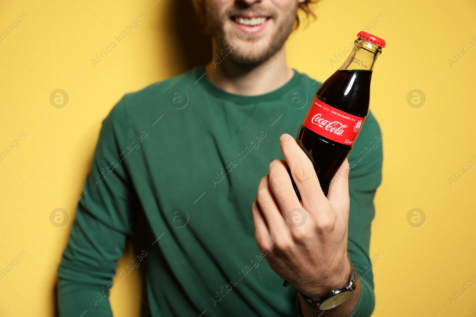 Photo of MYKOLAIV, UKRAINE - NOVEMBER 28, 2018: Young man with bottle of Coca-Cola on color background, closeup