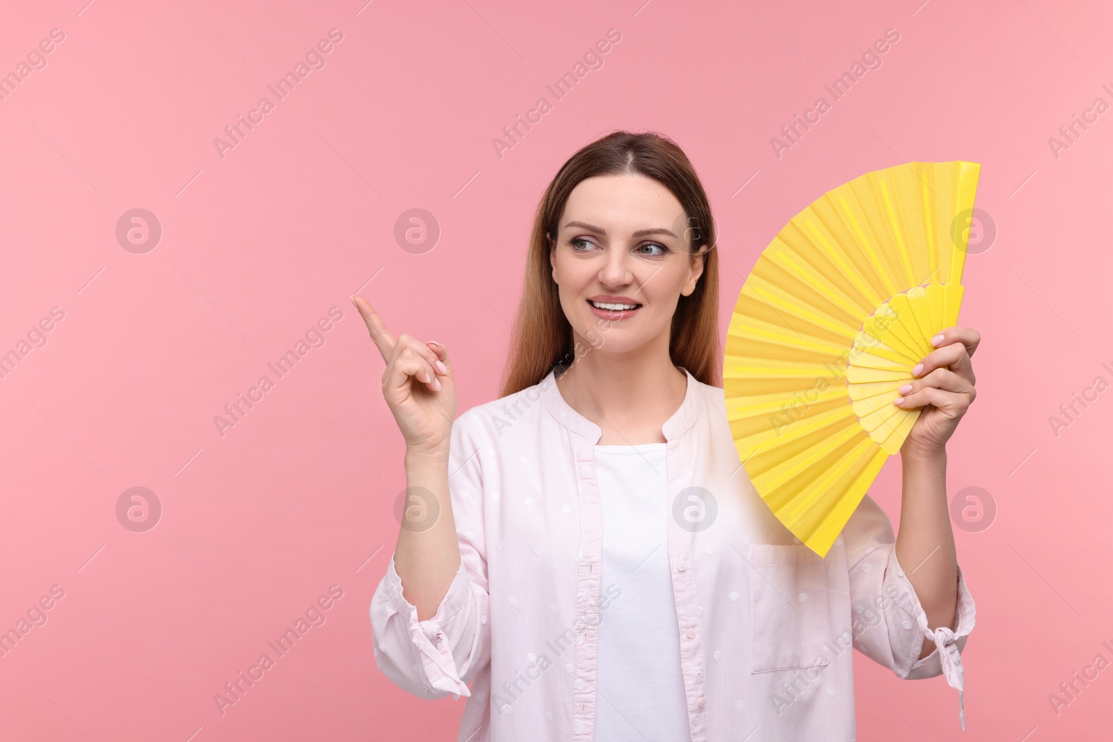 Photo of Happy woman with yellow hand fan pointing on pink background, space for text