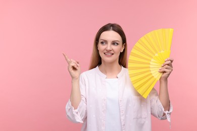 Happy woman with yellow hand fan pointing on pink background, space for text