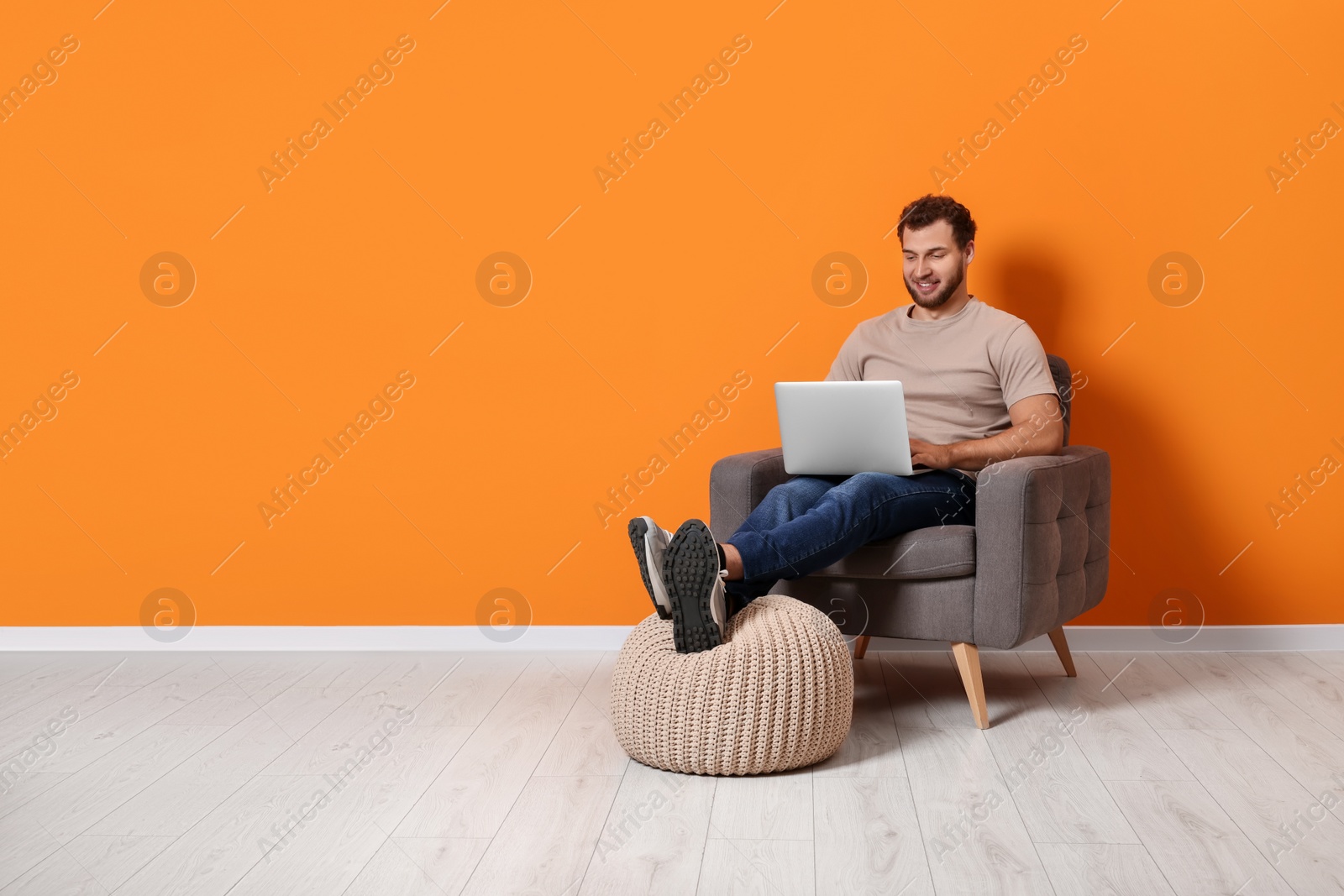 Photo of Young man using laptop while sitting in armchair indoors. Space for text