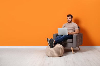Photo of Young man using laptop while sitting in armchair indoors. Space for text