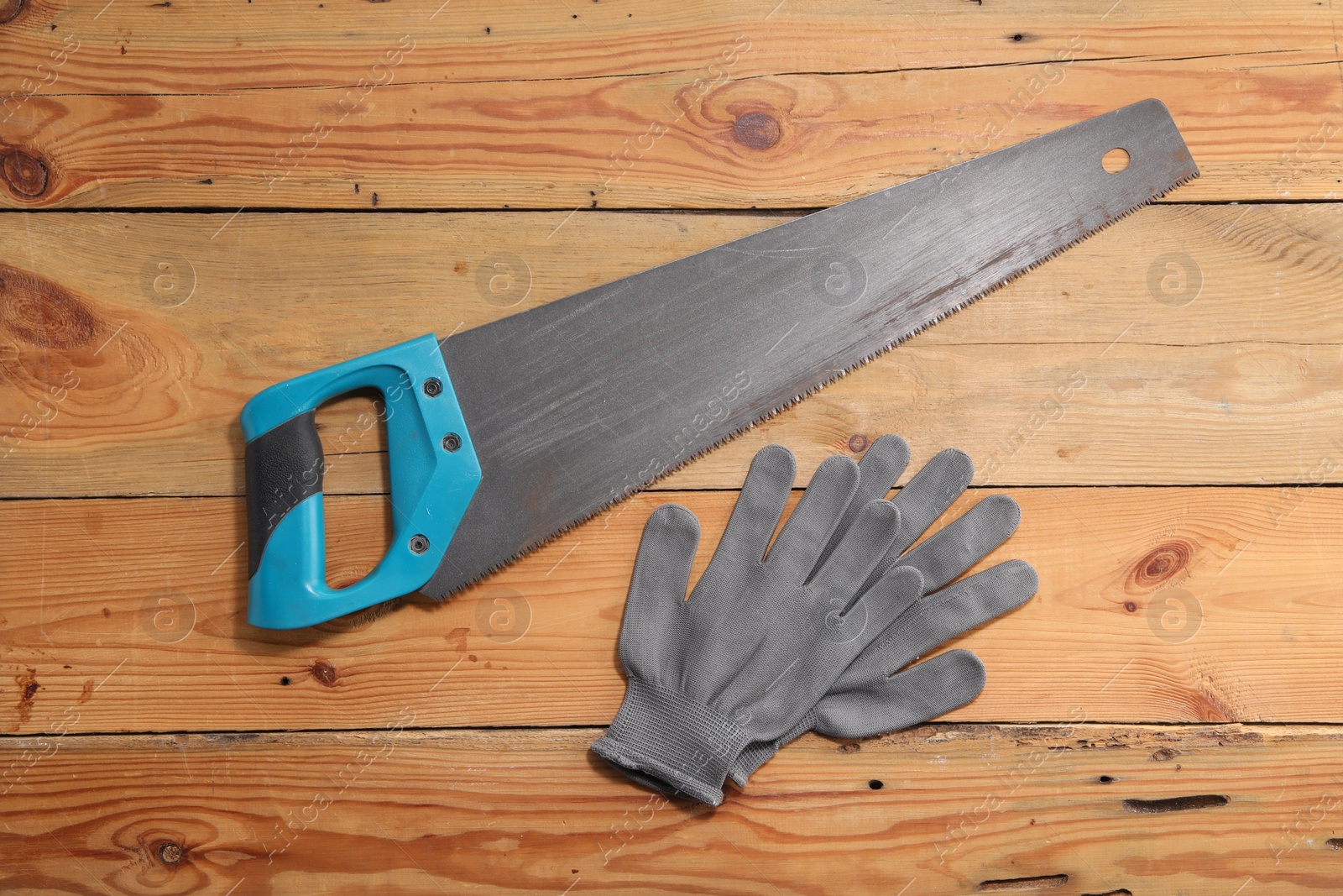 Photo of Saw with light blue handle and gloves on wooden background, flat lay