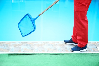 Photo of Male worker cleaning outdoor pool with scoop net