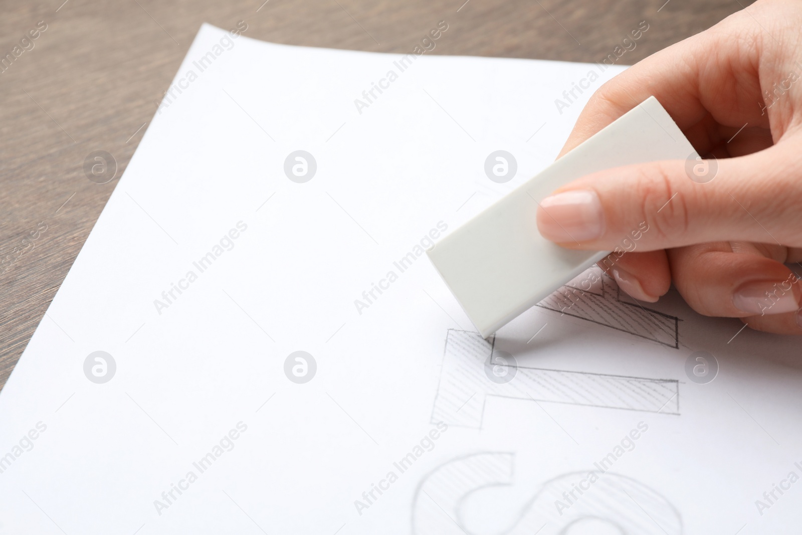 Photo of Woman erasing word on sheet of white paper at wooden table, closeup