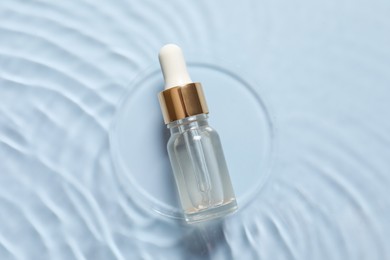 Bottle of cosmetic serum and water on light blue background, top view