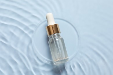 Photo of Bottle of cosmetic serum and water on light blue background, top view