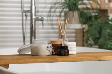 Photo of Wooden board with spa products on bath tub in bathroom, space for text