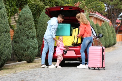 Photo of Young family loading suitcases in car trunk outdoors