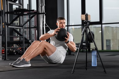 Photo of Man with ball streaming online training on phone at gym. Fitness coach