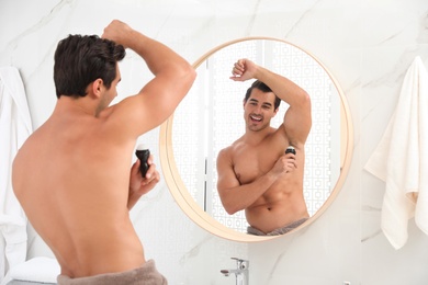 Photo of Handsome young man applying deodorant in bathroom