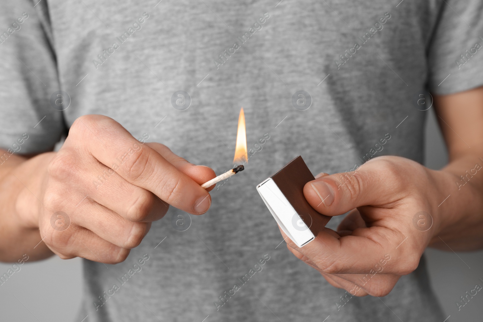 Photo of Man with box of matches on grey background, closeup