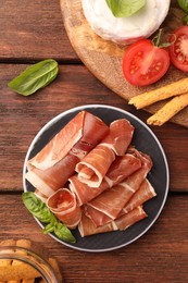 Rolled slices of delicious jamon and different products on wooden table, flat lay