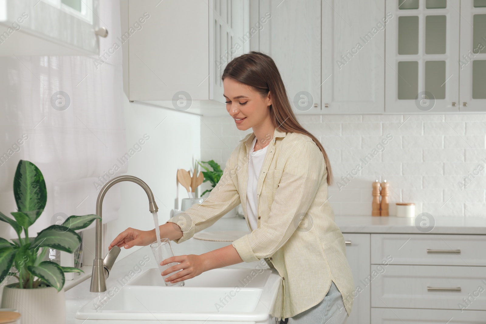 Photo of Woman filling glass with water from tap in kitchen