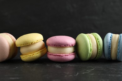 Many delicious colorful macarons on black table