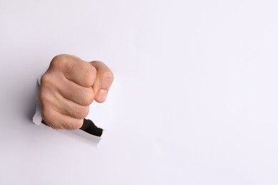 Man breaking through white paper with fist, closeup. Space for text
