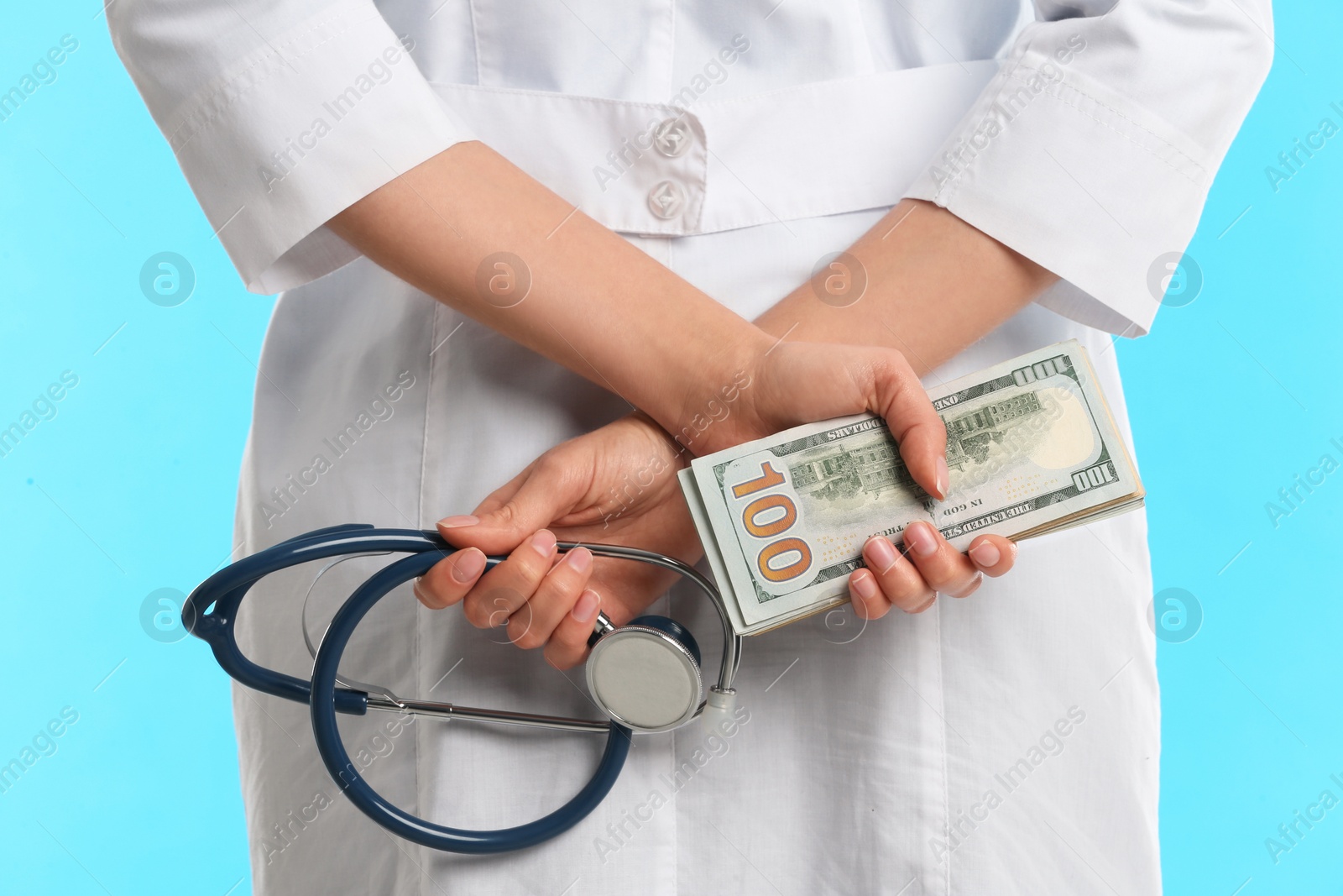 Photo of Doctor with bribe and stethoscope on light blue background, closeup. Corruption in medicine