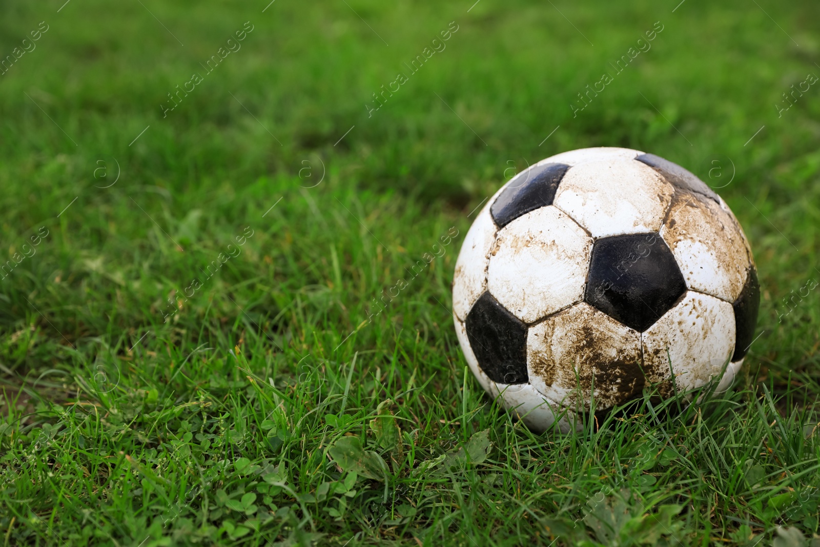 Photo of Dirty soccer ball on green grass outdoors, space for text