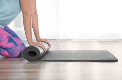 Photo of Woman rolling yoga mat on floor indoors, closeup. Space for text