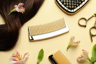 Hairdresser tools. Brown hair lock, combs, scissors and flowers on pale yellow background, flat lay