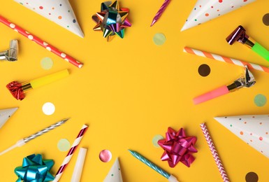 Photo of Frame of colorful blowers, party hats and other festive decor on orange background, flat lay