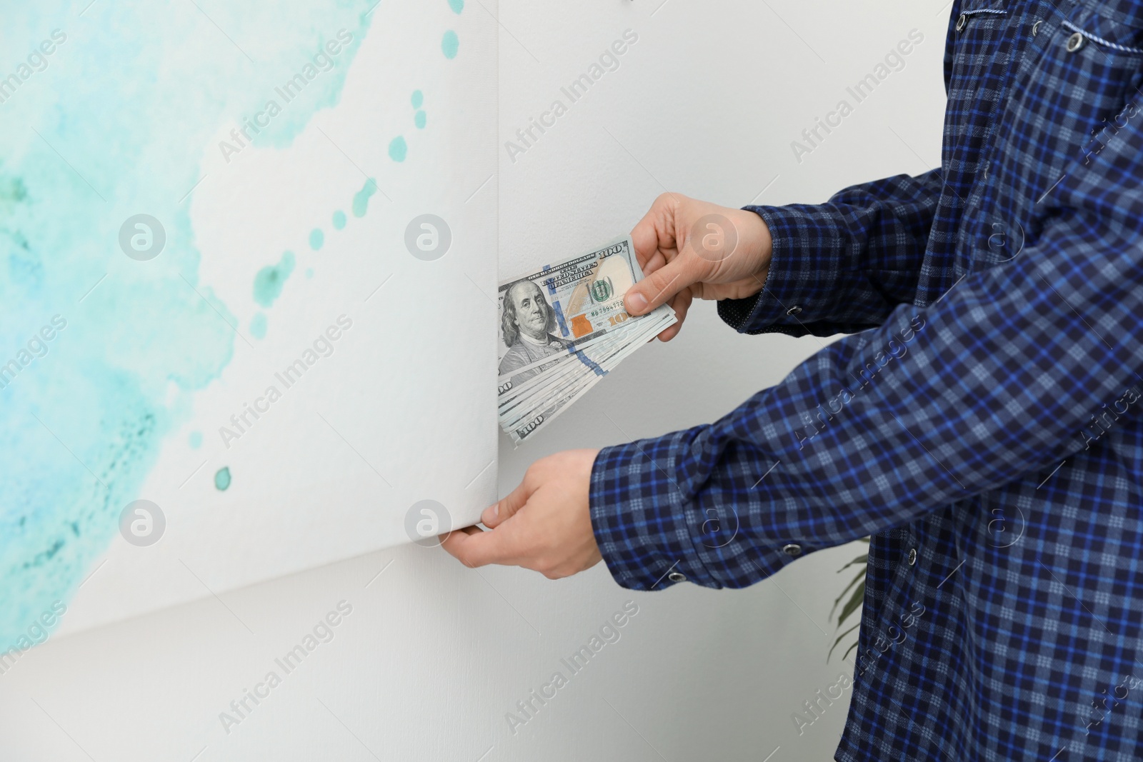 Photo of Man hiding dollar banknotes behind painting indoors, closeup. Money savings