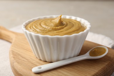 Bowl and spoon with tasty mustard sauce on light table