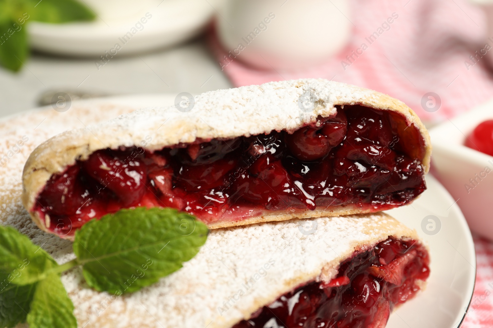 Photo of Delicious strudel with cherries, powdered sugar and mint on plate, closeup