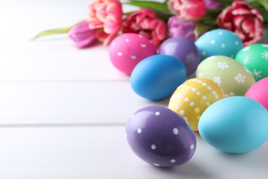 Colorful eggs and tulips on white wooden background, space for text. Happy Easter