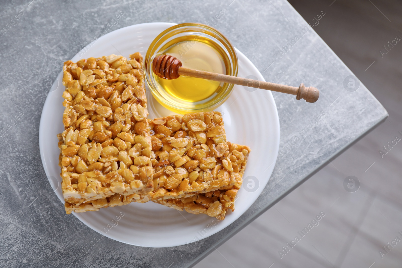 Photo of Delicious peanut kozinaki bars and honey on light gray textured table, top view