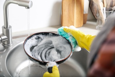 Photo of Woman washing dirty frying pan in sink indoors, closeup