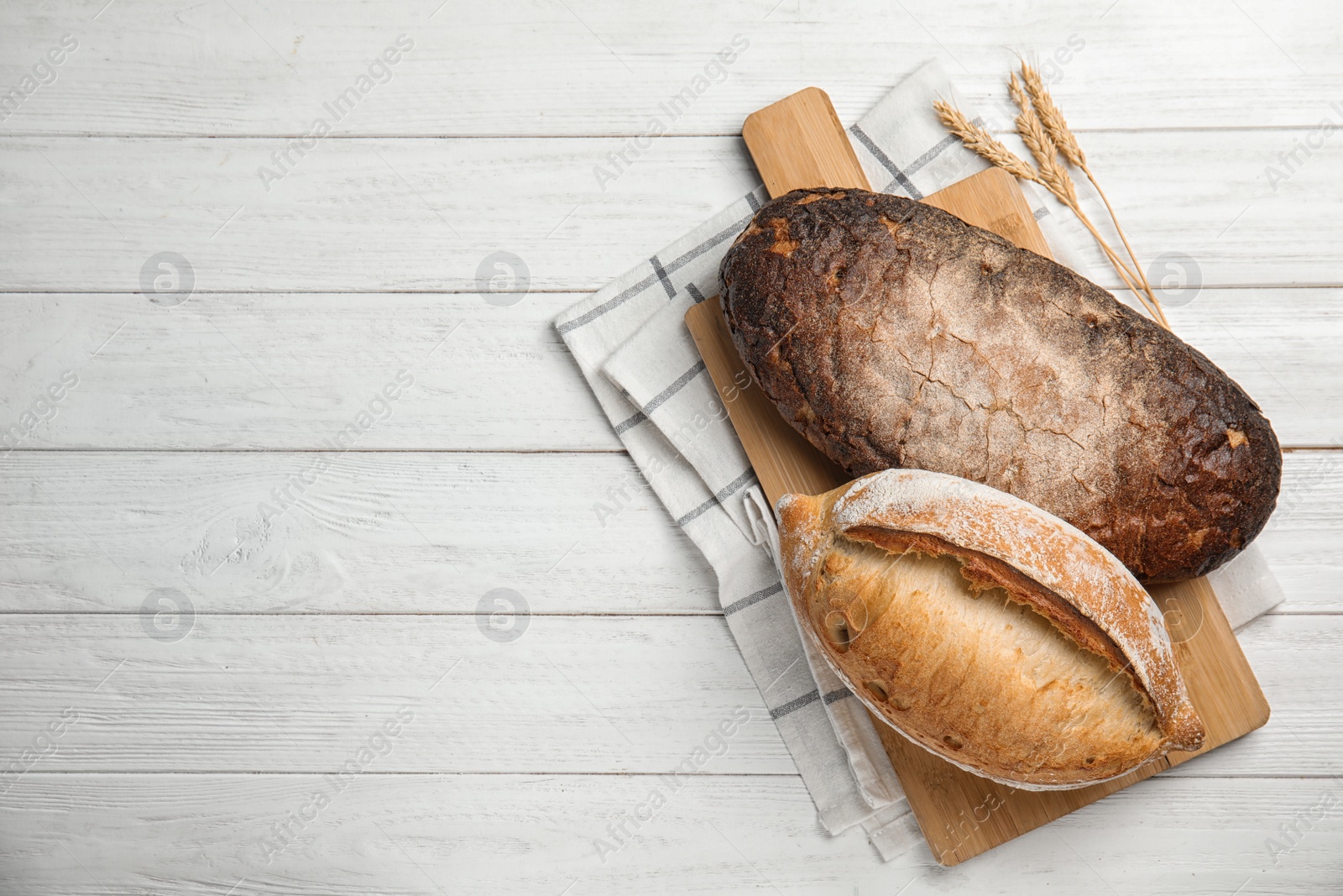 Photo of Board with loaves of bread on wooden table, top view. Space for text