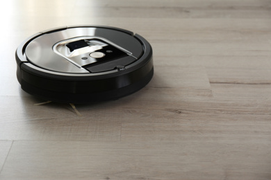 Photo of Modern robotic vacuum cleaner on wooden floor. Space for text